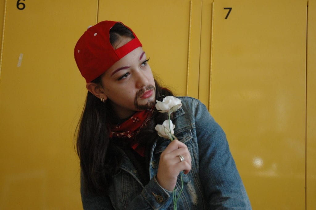 Student wearing a backwards red hat, a drawn on mustache, and holding flowers