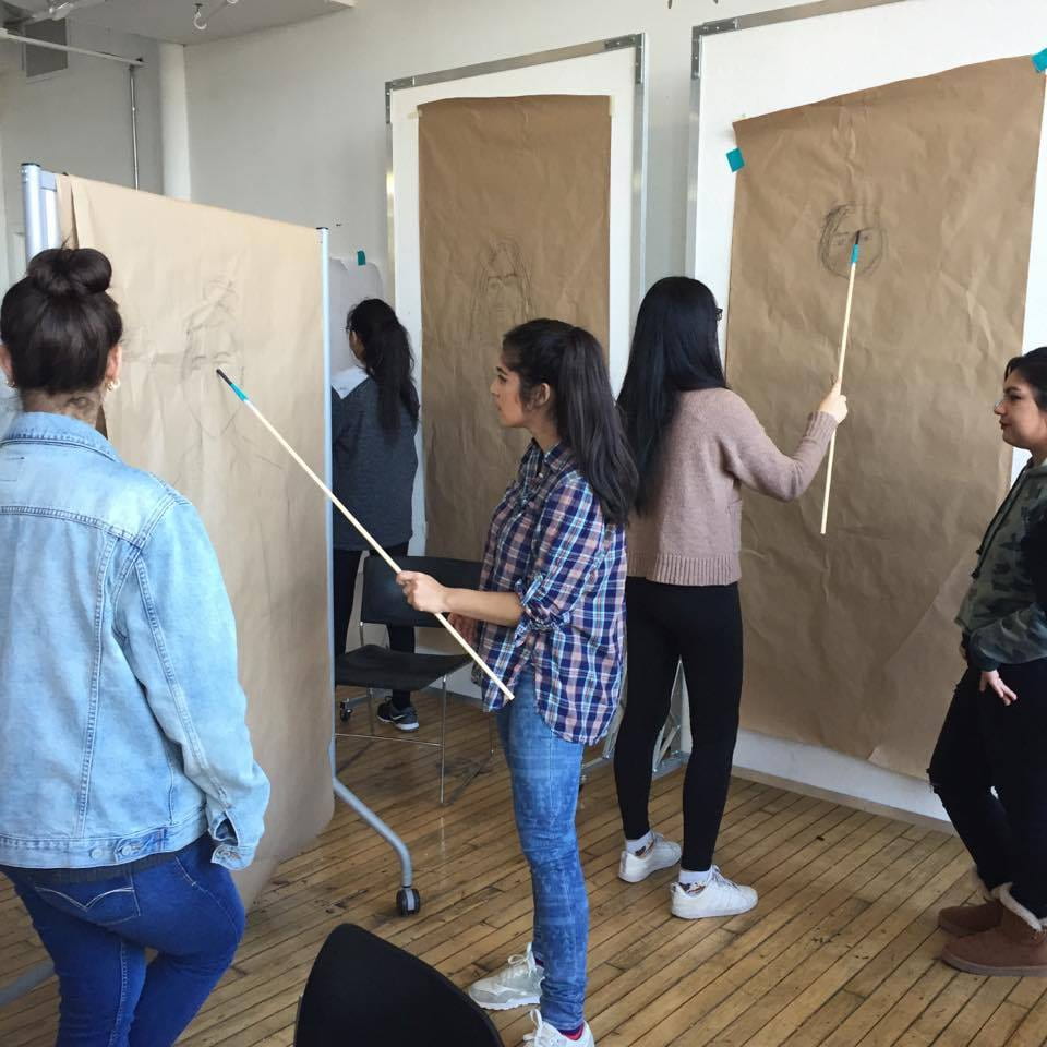 Students drawing portraits from a distance, with a crayon attached to a long stick. 