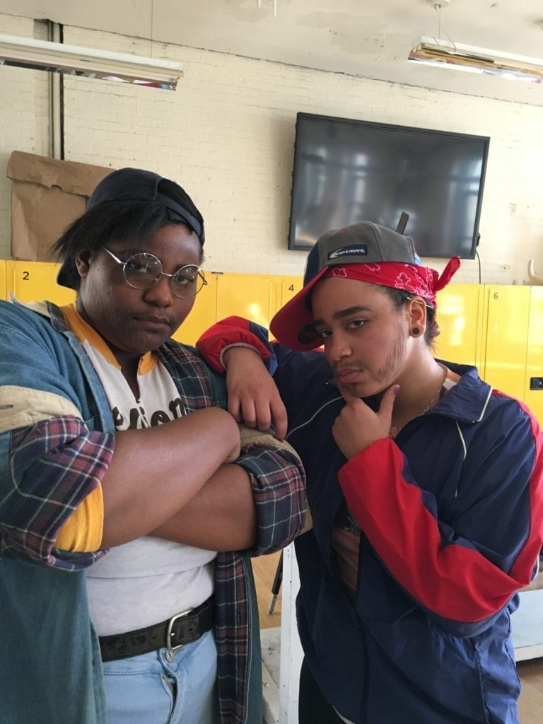 Students posing and wearing backwards hats and painted facial hair. 