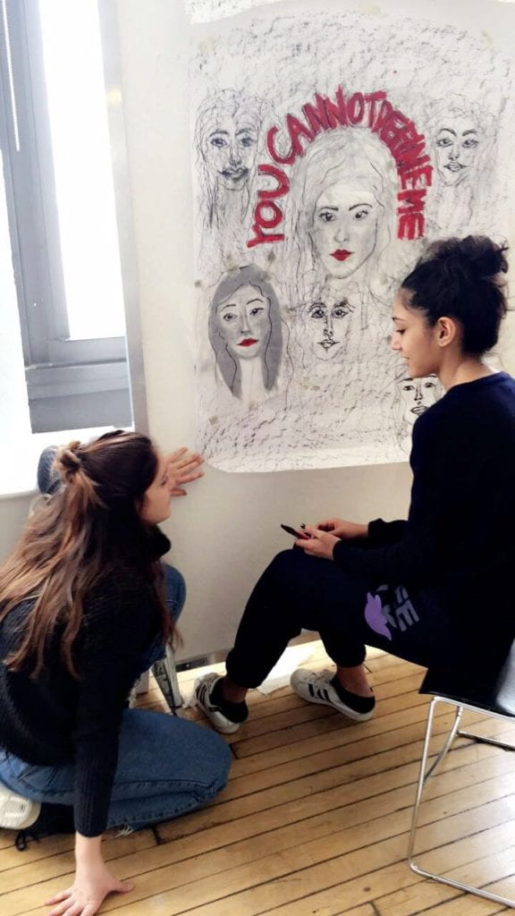 Two students working on an artwork that reads, "You Cannot Define Me."