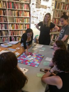 Image of a group of people sitting and standing around a table playing a board game