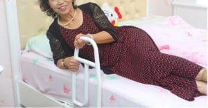 A woman is trying to get up by pulling up the handle with both hands. The handle is fixed on the right side of the bed.