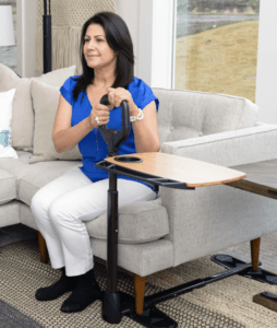 A person grabbing the handle of a device that has a tray attached while sitting on a couch.