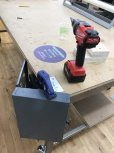 Hanging enclosure clamped to the corner of a table next to a screwdriver, hig, and plastic cup