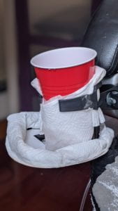 The image contains a cupholder prototype with a red cup inside and attached to the arm of a chair