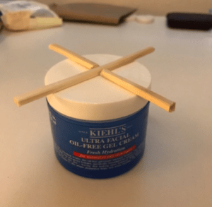 Intersecting chopsticks glued to the top of a plastic lid. Chopsticks are cut so they are in the shape of an "X" and their ends stick over the edge to give something to grip. 