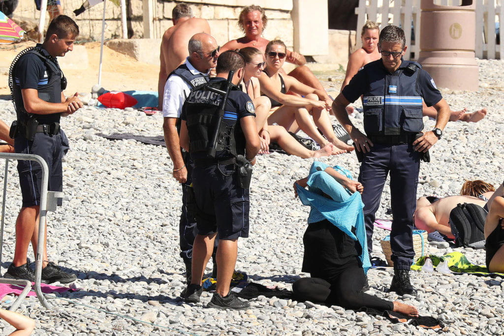 French police officers citing a woman wearing a Burqini on a French beach. Image Credit: Bestimage via NYTimes.