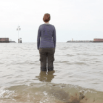 Close up of a fully clothed woman standing ankle deep in the ocean