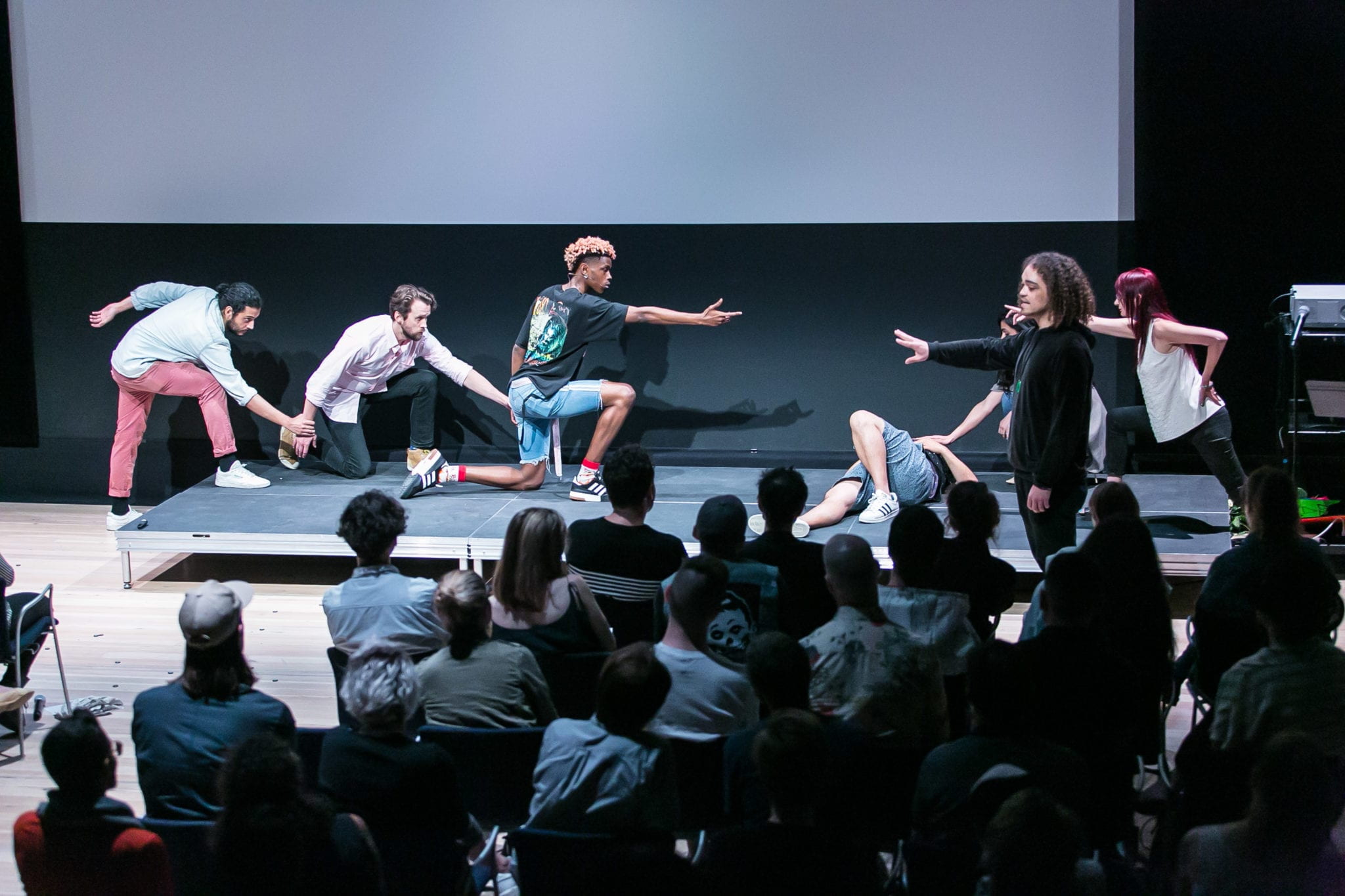 Seven people perform in a black box theater before an audience.