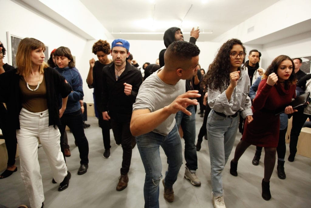 Multiple people in an art gallery leaning toward the camera with artist Shaun Leonardo in the front.