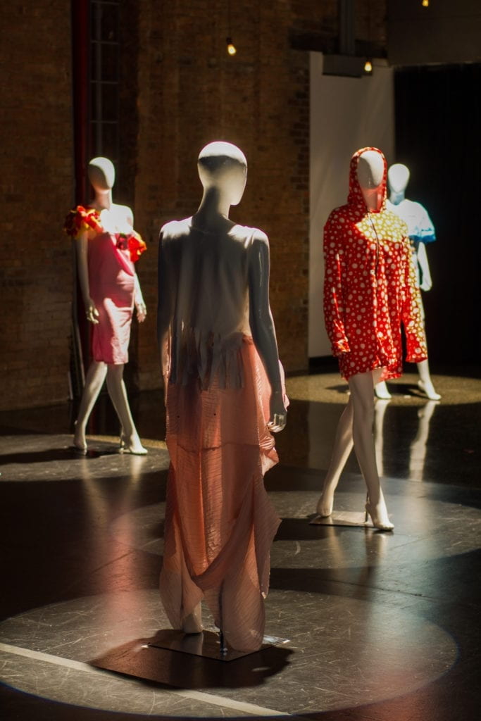 Four clothes mannequins stand in a dark space. Each has a single spotlight from above directed at them.