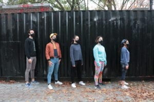 Five members of the dance troupe stand in a descending line with masks on