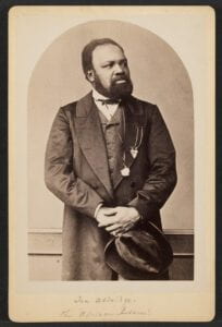 Black and white photo of Ira Aldridge, a bearded ABlack man in an elegant suit holding a hat looking to the right. 