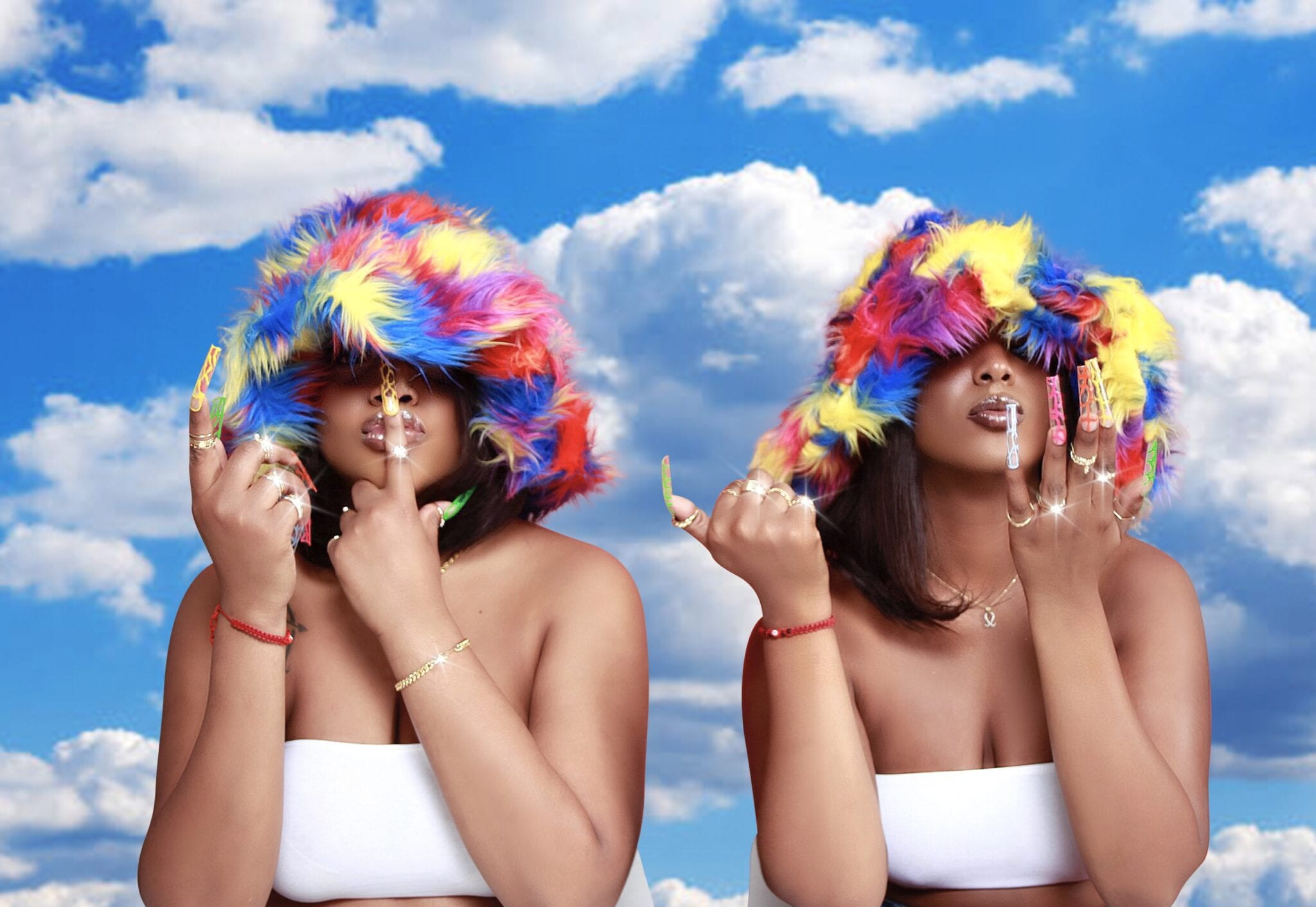 Photograph of two women with colorful, feathery hats on and long nails in front of an artificial looking background of clouds