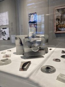 A installation image of resin camera that contains broken camera pieces, placed on top of a white pedestal.