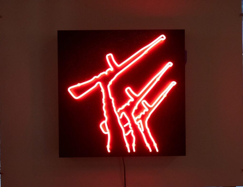 Image of interior of gallery featuring a red neon sign depicting hands holding guns