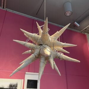 Photograph of a spike sculpture made from paper, suspending from the ceiling with yarn. 