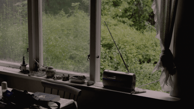 Video still of a room with a large window that overlooks a scenic green forest area. 