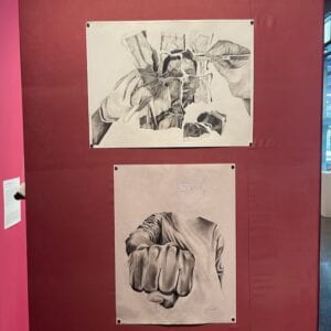 Two black and white pencil drawings hung parallel to each other. Each drawing has a figure, one of which depicts a conservator reconstructing a photograph and the other drawing depicts a man with his fit highlighted to the viewer. 