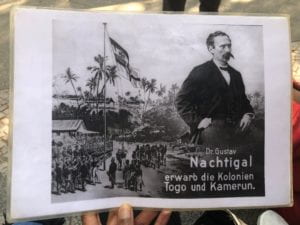 In the background is a village--either in Togo or Cameroon--where villagers are watching the German Empire flag being raised in the background. Dr. Nachtigal was key in acquiring these colonies.