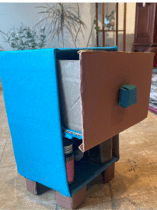 Side view of a shelf with a drawer that appears to be about 2 feet tall. The sides are pained blue and the drawer has a blue handle on it.