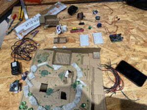 Disassembled cardboard mechanism with motors, servos, wires, breadboards and arduino