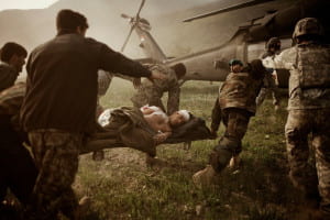 Injured soldier on stretcher being carried to helicopter by other soldiers