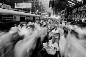 two men read the newspaper in transit station as commuters move around them