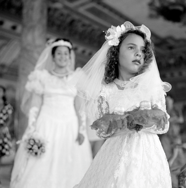 Young girl in elaborate flower girl dress with bride in the background