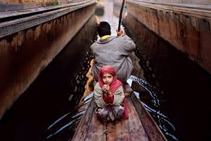 Father rows boat while young girl looks pleadingly at camera