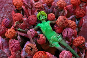 Man in green powder is held by others covered in red powder