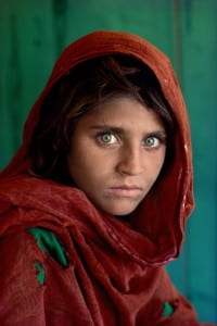 Girl with head covering staring intensely at camera with bright green eyes