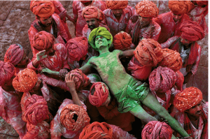 Man covered in green powder is held by others covered in red powder