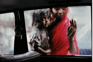 Two children look into car window, one is dressed all in red