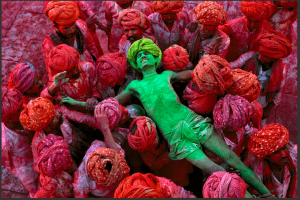 Man covered in green powder held by others covered in red powder