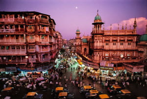 Purple skies surround pink buildings with cabs and people below