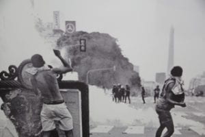 historic photo of protestors and police on street with large smoke fire in background