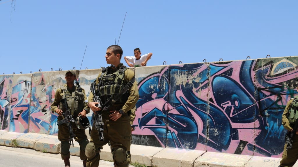 boy looking over graffiti wall at two soldiers