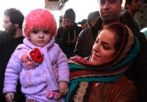 Iranian woman holding her child and smiling in crowd.