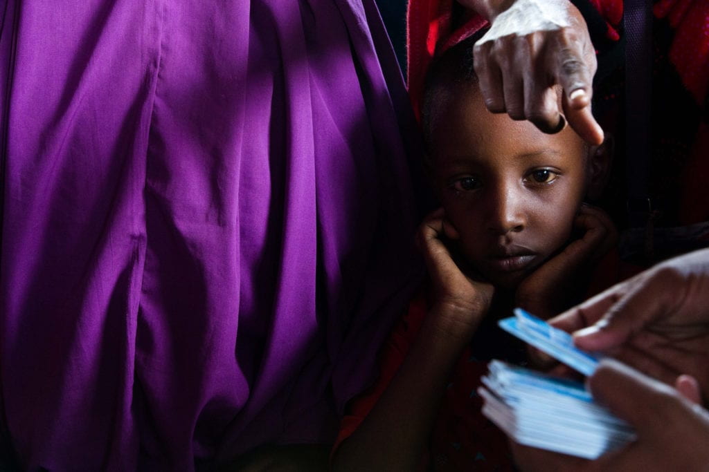 a young boy waits while his mother tops up her SCOPE Cash-Based Transfers. 