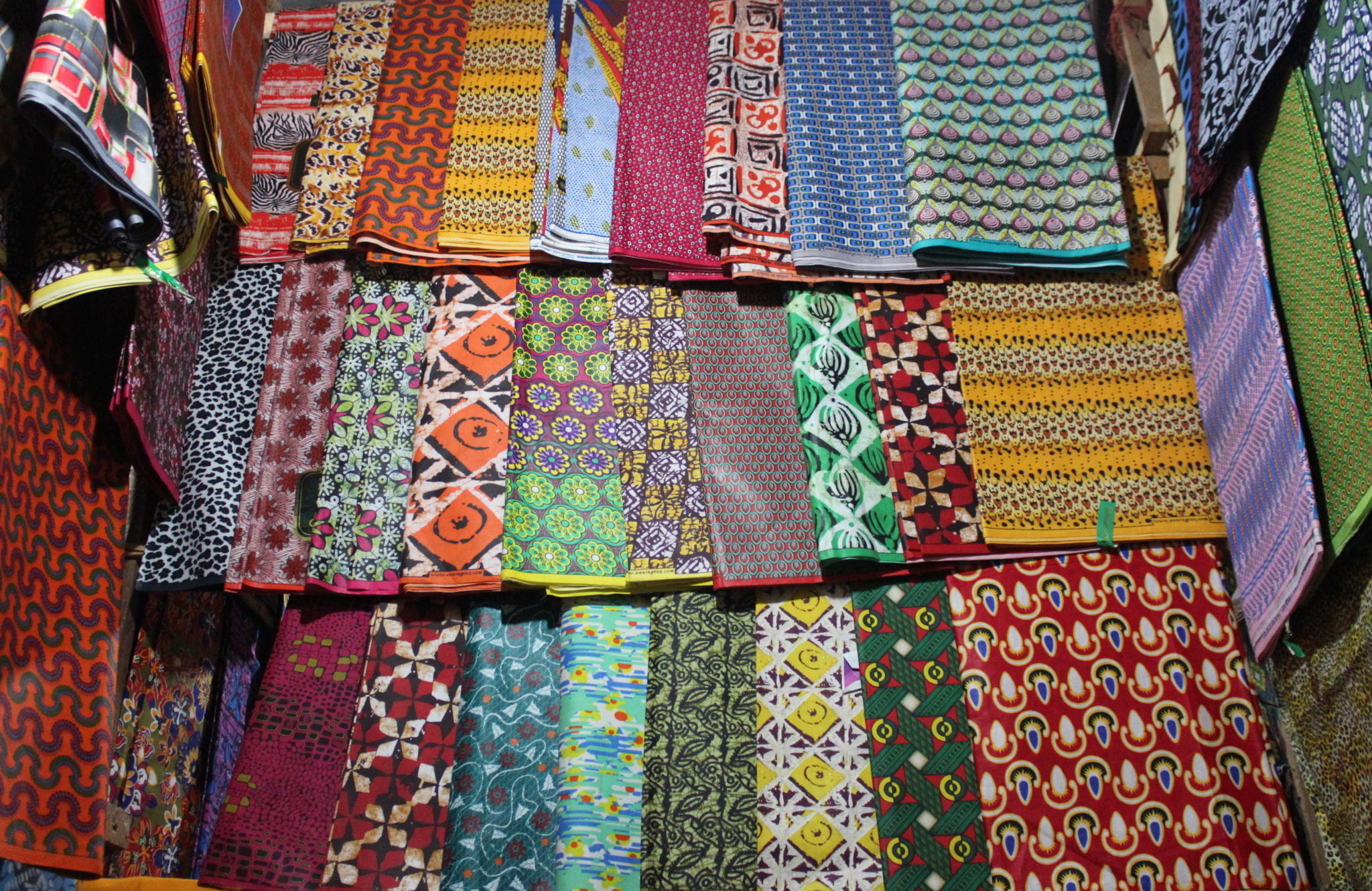 Traditional fabrics with intricate and colorful patterns spread out in stall.