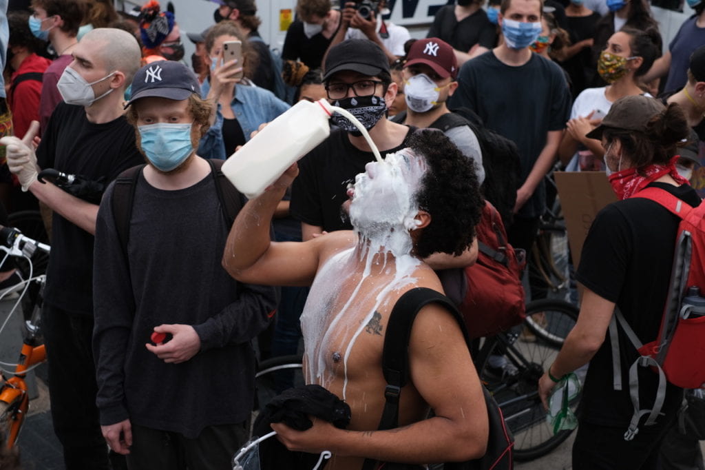 man pouring milk on his face amongst a crowd of protesters