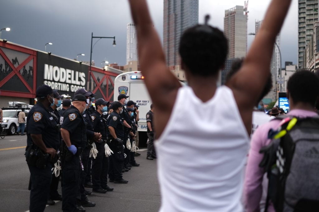 man with arms raised in forefront before a line of police