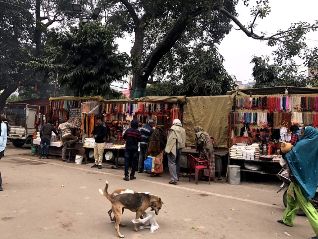 people manning stands full of wares on a street where dogs play