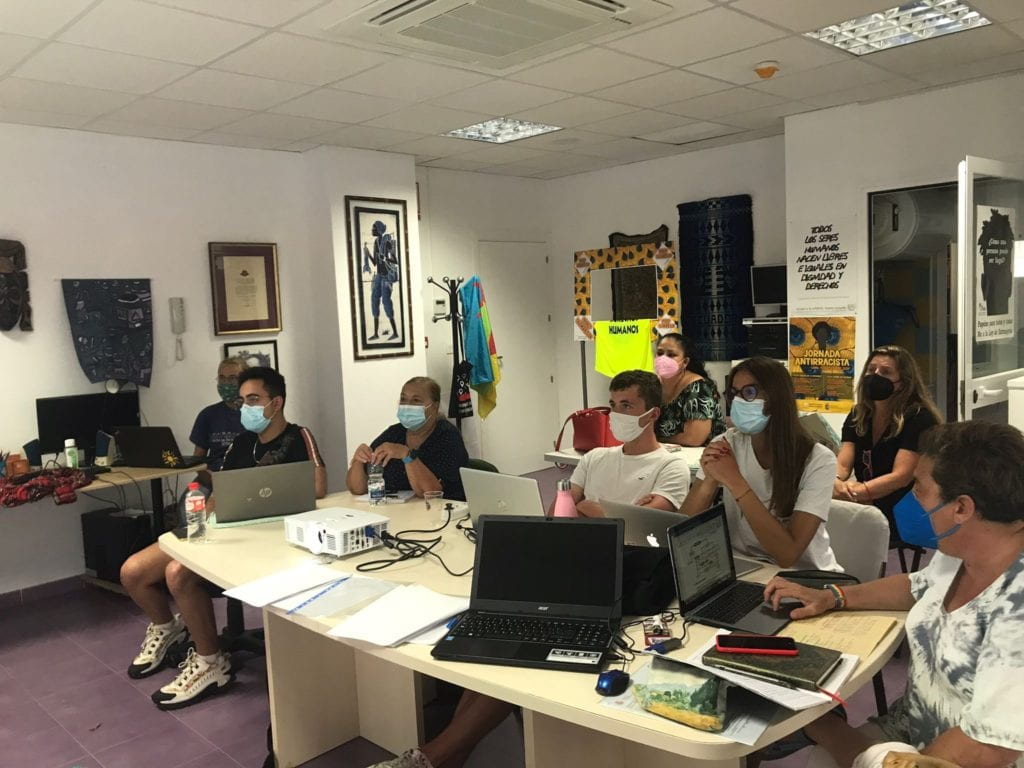 masked people sitting at a large desk with laptops