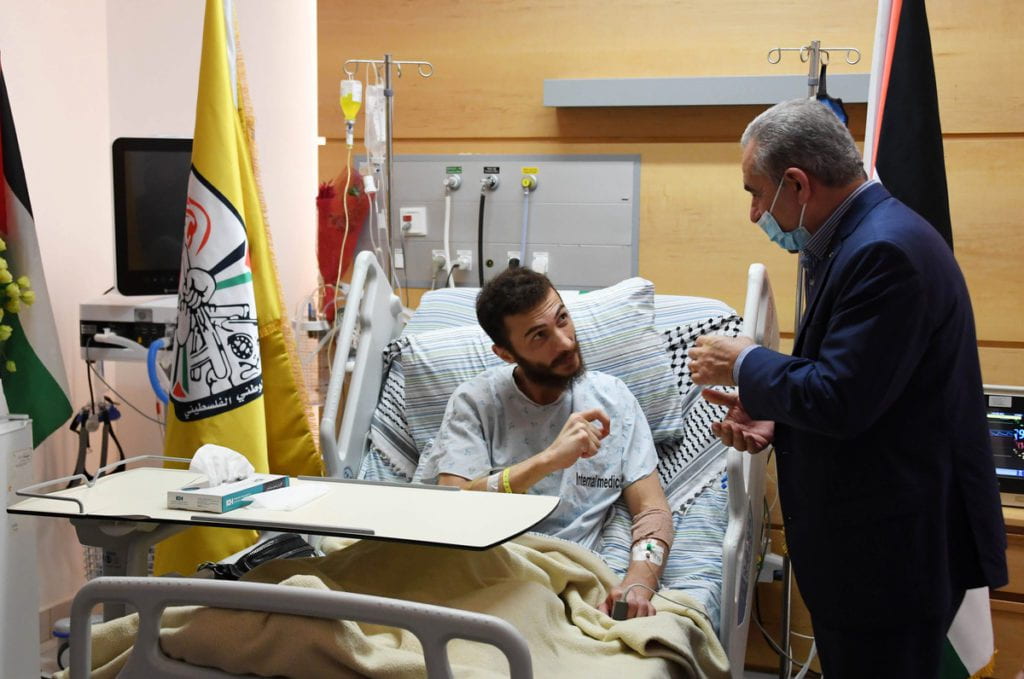 man in hospital bed speaking to man in suit