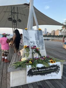 A memorial altar to Sylvia Rivera and Marsha P. Johnson. A black and white image of the two activists is propped up with flowers laid out in front of the photo.