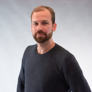 Man in gray sweater with a reddish beard looks at the camera.