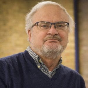 Gentleman with gray hair and glasses smiles at the camera.