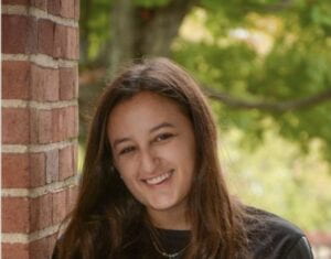 Portrait of a woman with brown hair smiling from shoulders up, wearing a black top. 